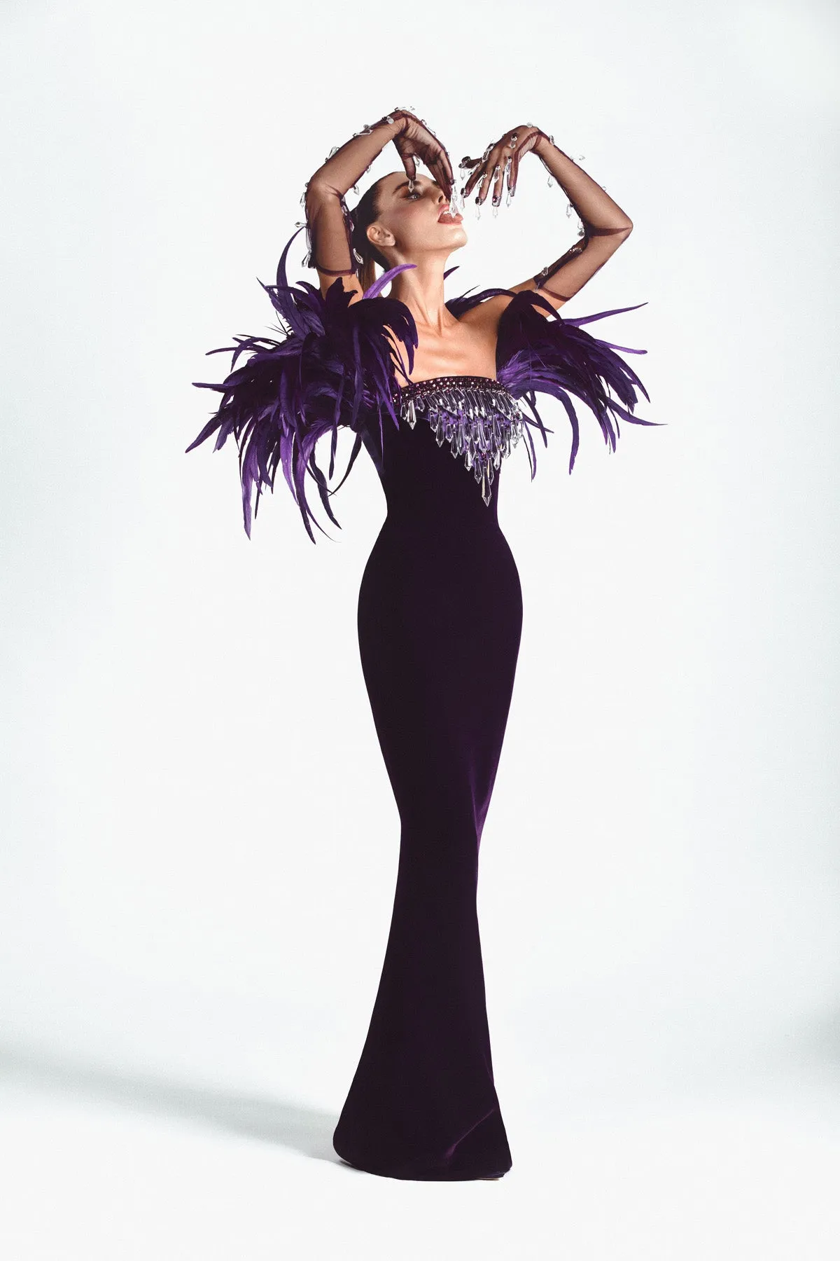 Purple velvet strapless gown, hand embroidered with Swarovski stones, crystal spikes, and finished with coq plumes. Worn with tulle gloves embroidered with stones and dripping crystals